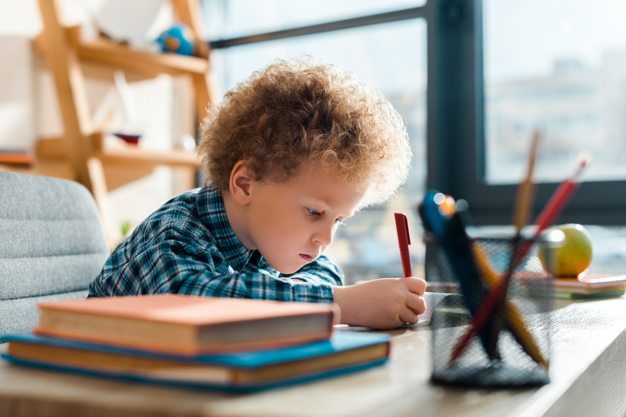 selective focus of curly kid writing near books